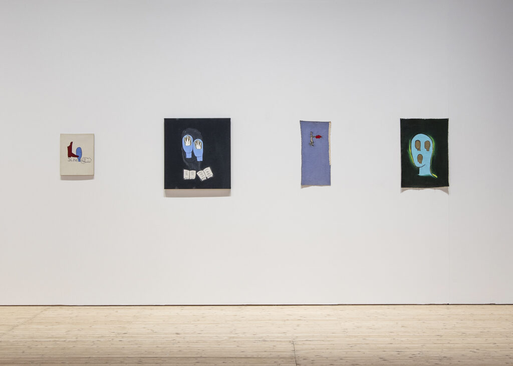 Row of works in blue, red and green on textile and canvas hangs on a white wall.