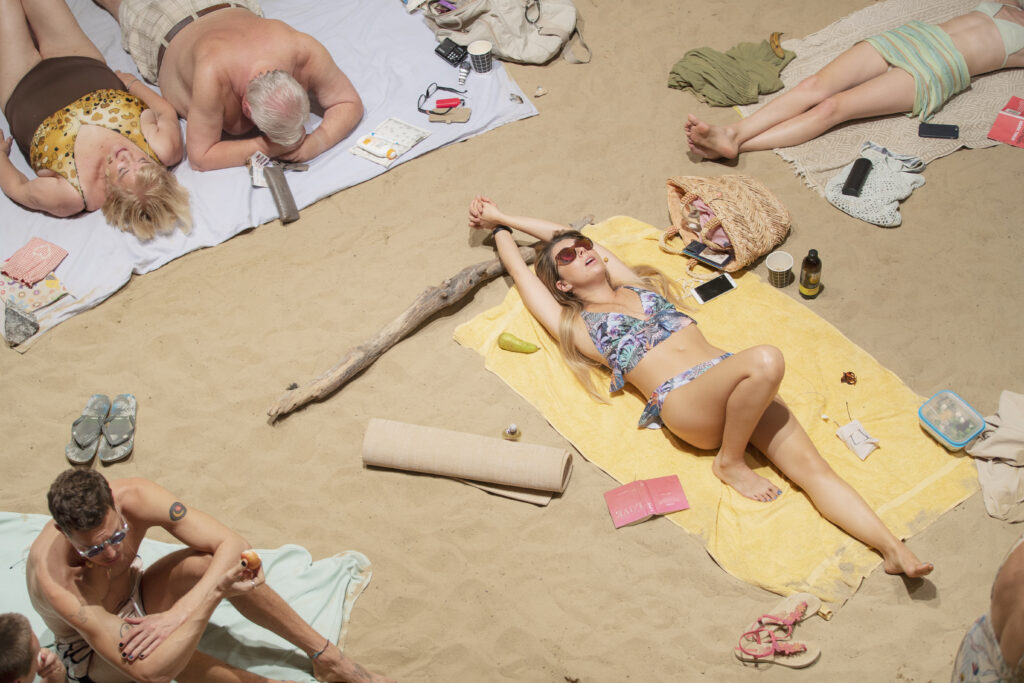 A close-up picture of some people singing and lying on a sandy beach in pastel-colored swimwear.  