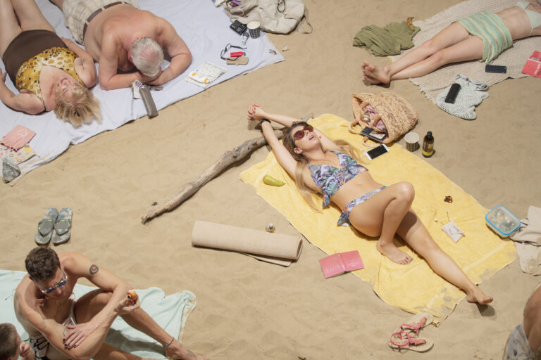 Närbild av några personer som ligger på en sandstrand och sjunger i pastellfärgade badkläder.