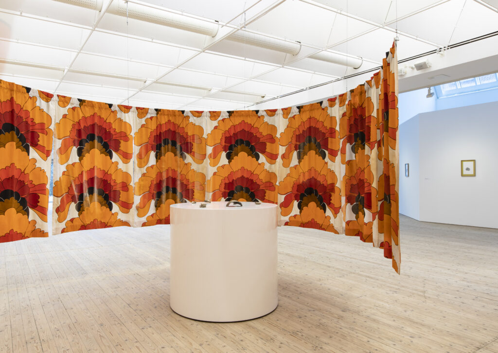 Image of a 70s curtain in red and orange hanging around a round podium in Ann Böttcher's exhibition.