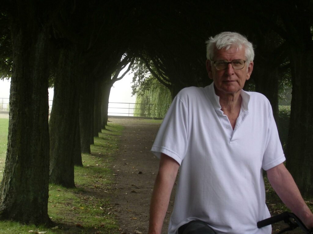 Porträtt av Lasse Söderberg ståendes i grön trädallé