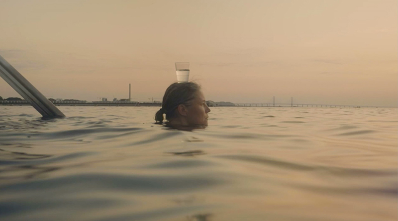 Kvinna i havet, enbart huvudet sticker upp balanserandes ett glas vatten