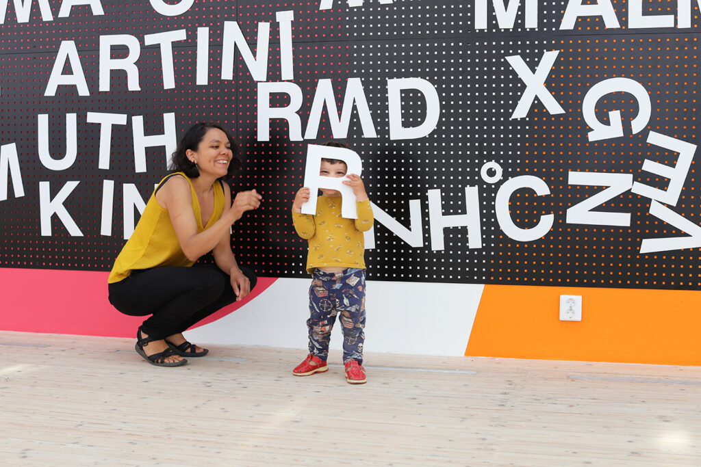 Mamma och barn framför ett av Luca Freis verk med stora magnetiska bokstäver i konsthallen.