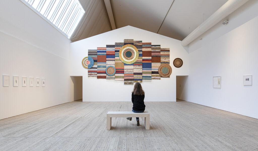 Ljusschaktet i konsthallens utställningsrum med Ann Böttchers färgrika verk gjort av mattrasor.