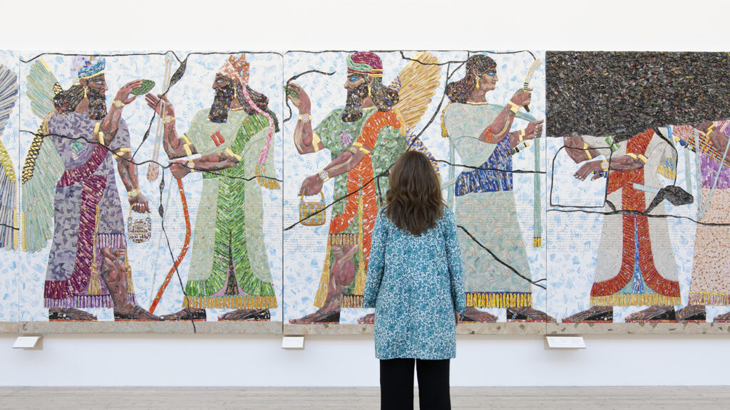 Image of a woman standing in front of and looking at one of Michael Rakowitz's colorful works.