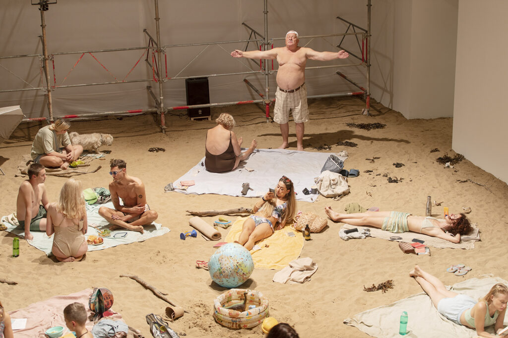 Bild tagen uppifrån på en artificiell sandstrand fylld av människor på pastellfärgade handdukar.