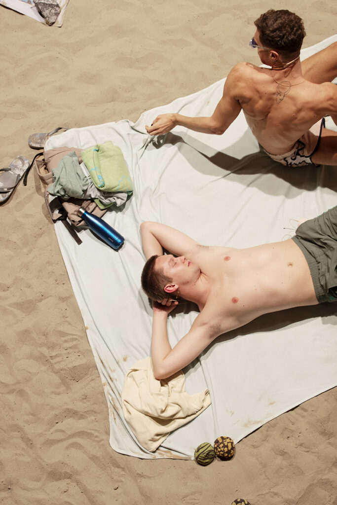 Picture taken from above of two young men on a towel at a sandy beach.