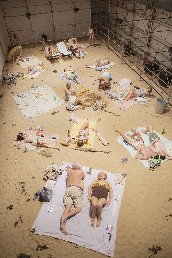 Picture taken from above of an artificial sandy beach filled with people on pastel-colored towels.