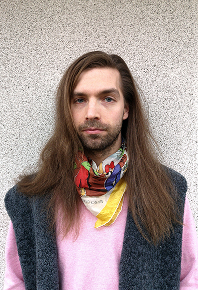 Porträttbild av konstnären Mattis Sumari i rosa tröja och mörk väst.