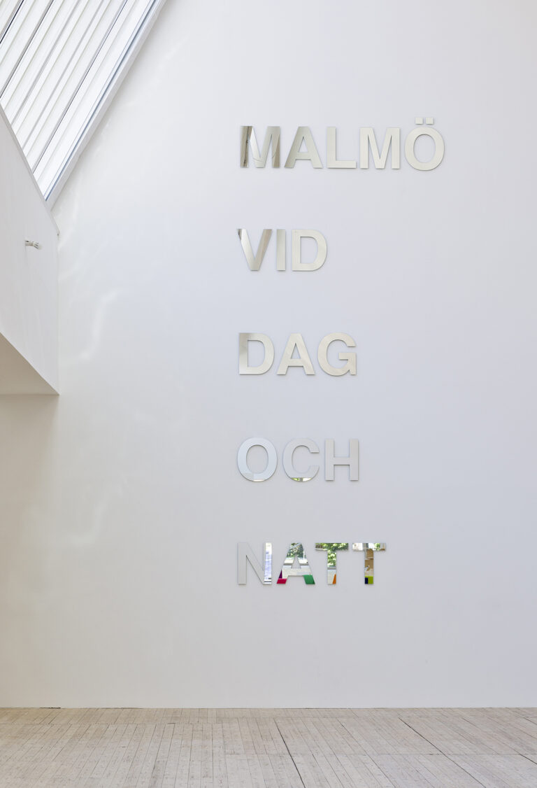 Texten "Malmö vid dag och natt" gjord av speglar på väggen i konsthallen