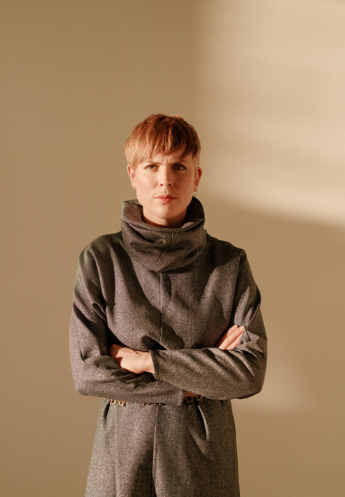 Portrait of a serious Ragna Bley in front of a window where sunlight streams in.