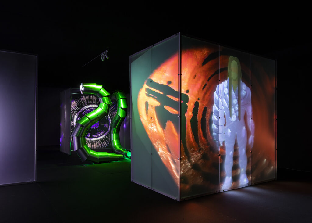 A work inspired by science fiction featuring a large light cube in the foreground with a figure resembling a video game character. In the background, there are large metal pipes in front of an eye. The color palette is purple, green, blue, and black.