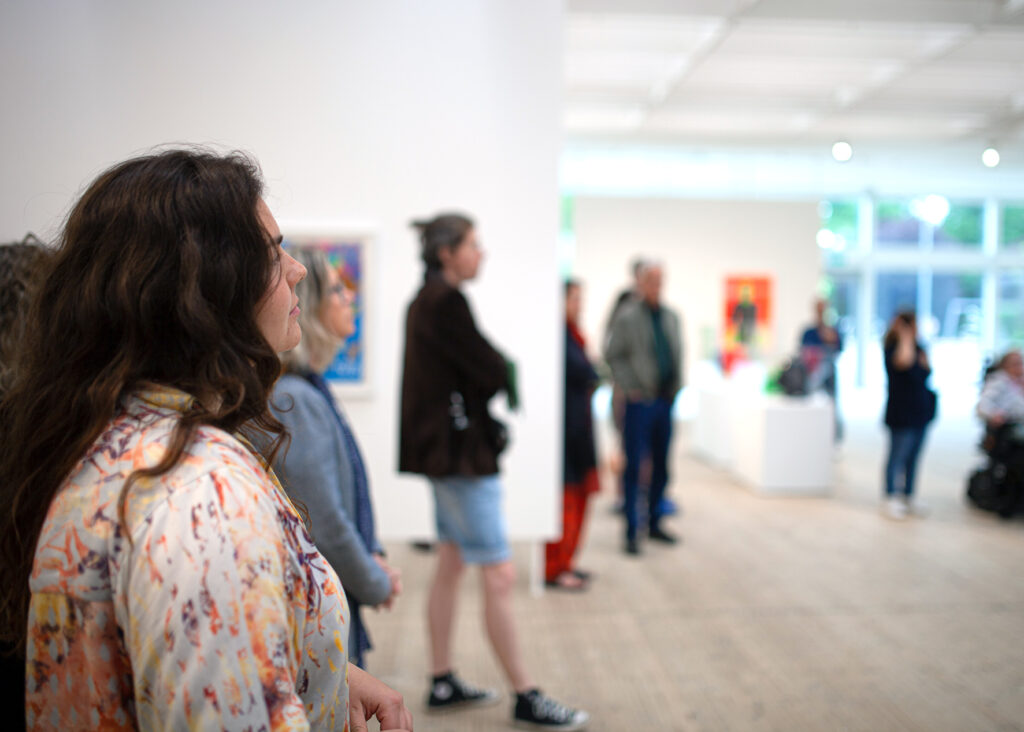 People stand in the exhibition and listen to someone speaking.