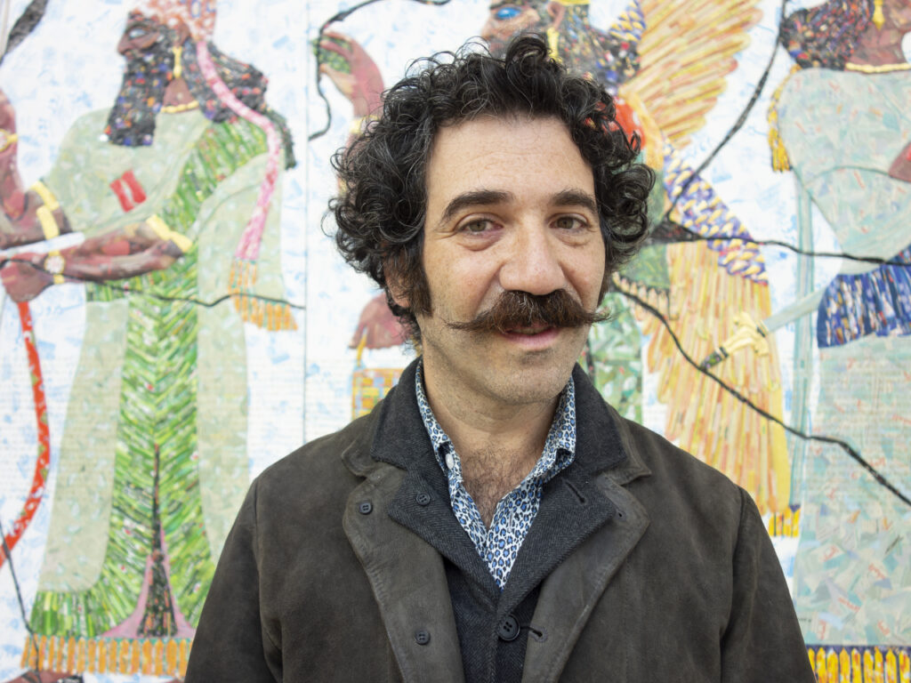 Porträttbild av konstnären Michael Rakowitz som står framför ett av sina verk i konsthallen