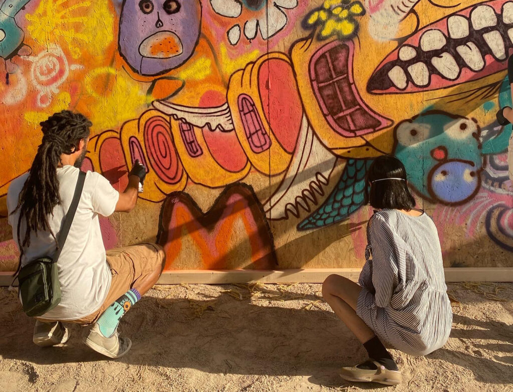 Bild tagen bakifrån av Kim Demåne och en ungdom som spraymålar en vägg