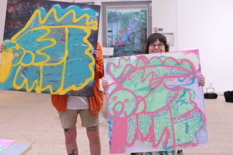 Två personer visar upp konstlyftets glada målningar