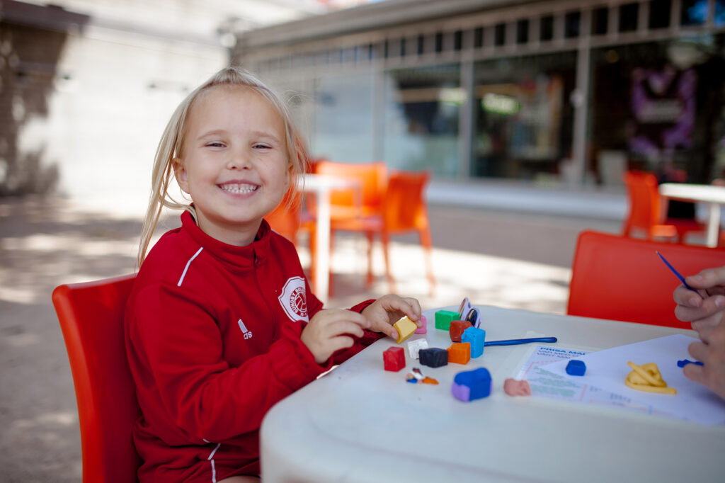 Glad liten tjej i röd tröja skapar i konsthallens uteverkstad.