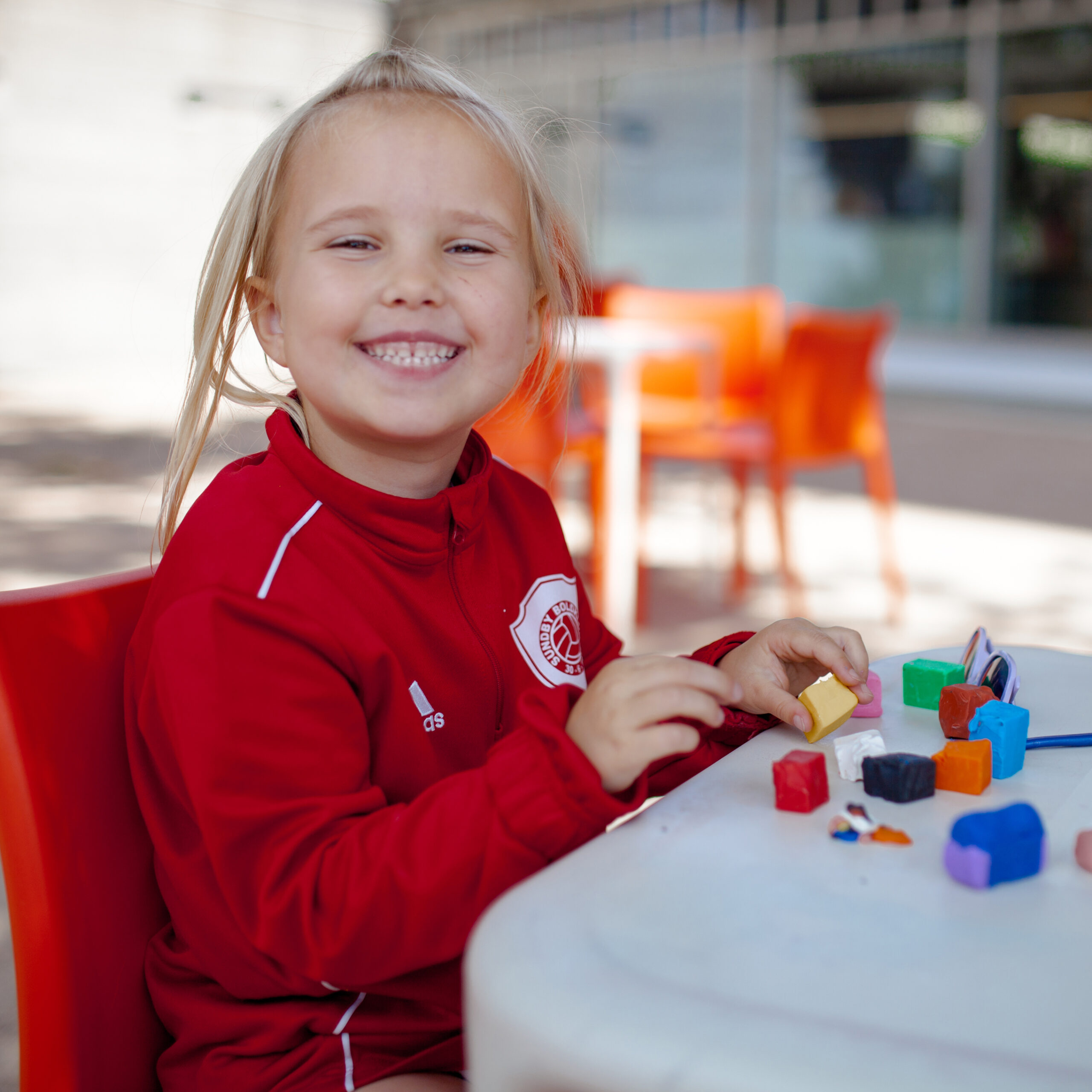 Glad liten tjej i röd tröja skapar i konsthallens uteverkstad.