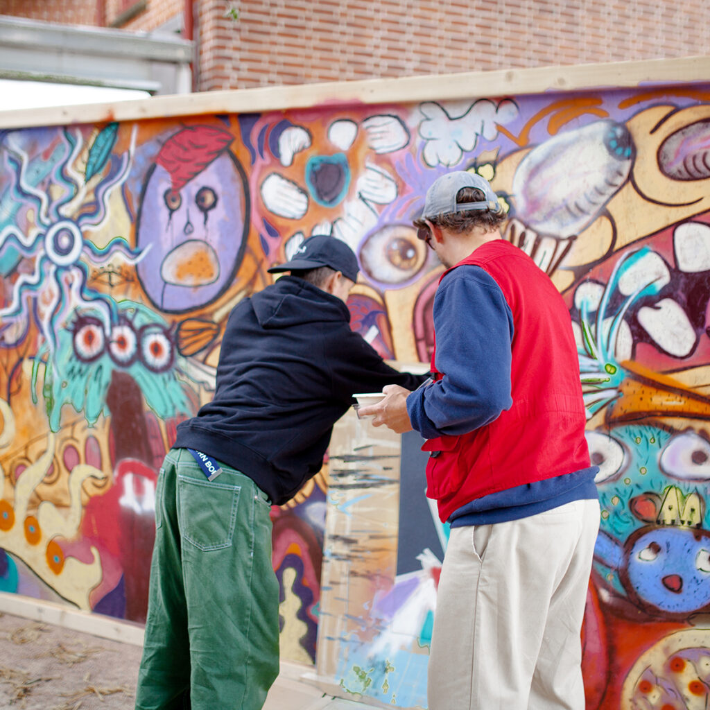 Två killar målar graffiti i glada färger på en temporär vägg utanför konsthallen