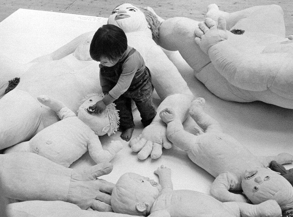 Svartvit bild av litet barn som leker bland stora dockor i tyg