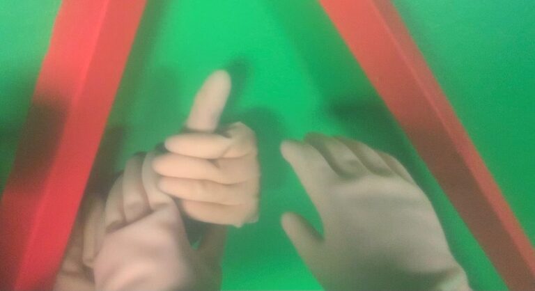 Abstrakt och suddig bild i grönt och rött av händer med plasthandskar som tar på varandra