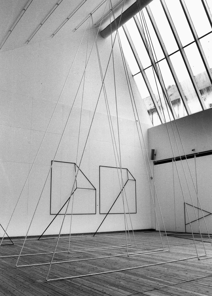 En bild från utställningshallen. Konstverk i form av tjocka trådar sitter uppspända i tak och längs väggar i olika former.