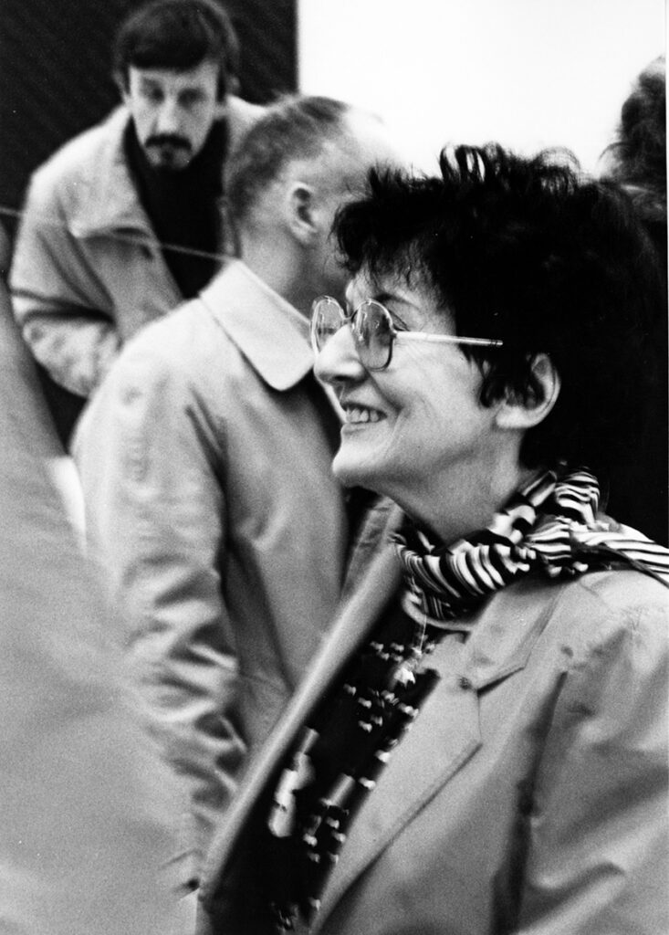 En bild i rörelse en kvinna ler mot någon utanför bilden, i bakgrunden skymtar fler personer.
