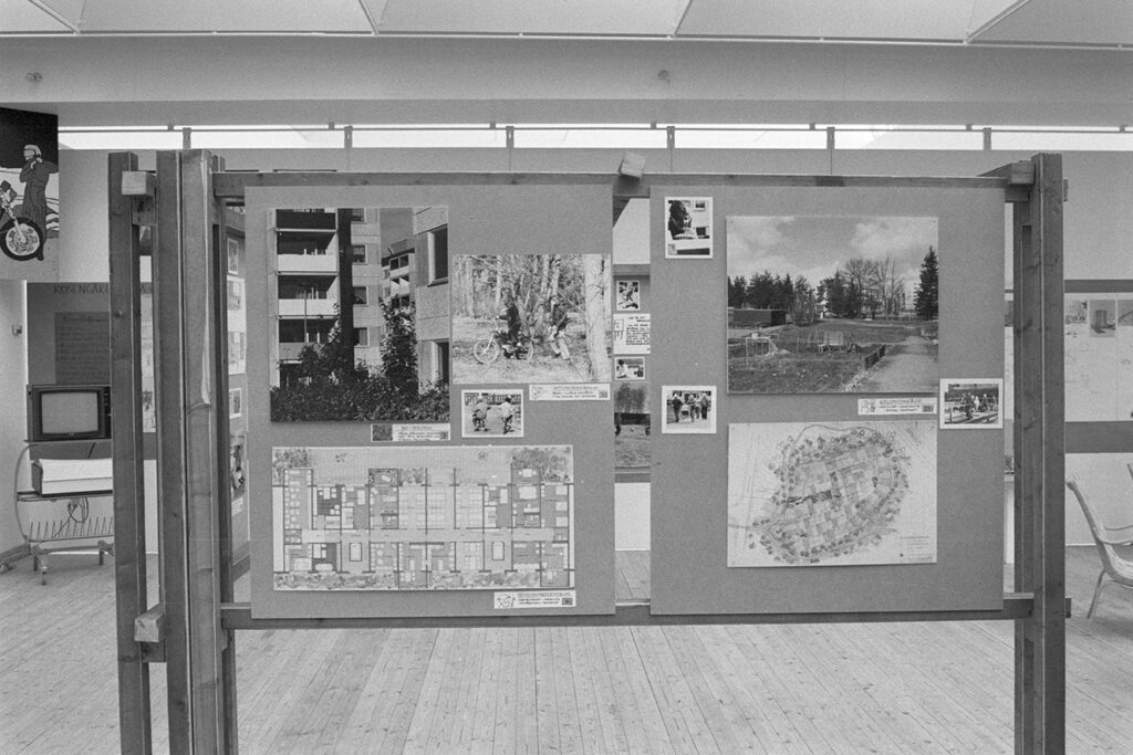 En tavla uppställd i utställningshallen. På tavlan sitter olika fotografier och kartor.