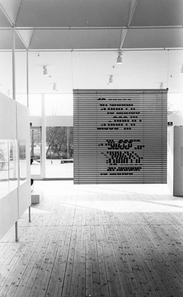 Utställningshallen under utställningen TECKEN. Centrerat i bild syns en persienn som har former tryckta på sig.