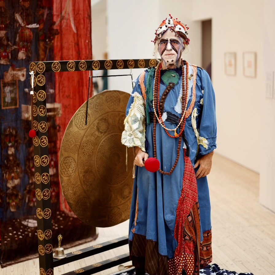 Porträtt av konstnär vid en gong, klädd i klara färger och smycken