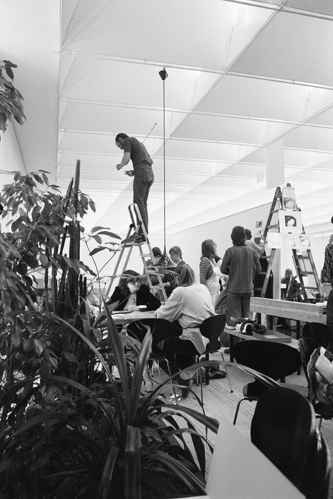 Ett antal människor gör förberedelser inne i utställningshallen. I förgrunden syns några växter. En person står högst uppe på en stege.