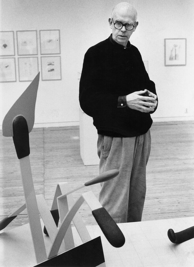Claes Oldenburg står i utställningshallen och kollar på ett konstverk som föreställer tändstickor.