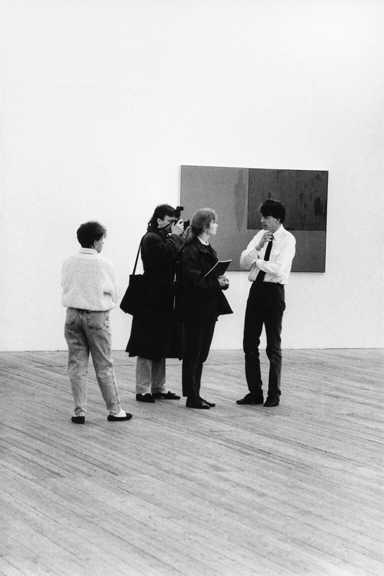 Fyra personer står i utställningshallen. En tavla på väggen i bakgrunden. En finklädd person blir intervjuad och fotograferad.