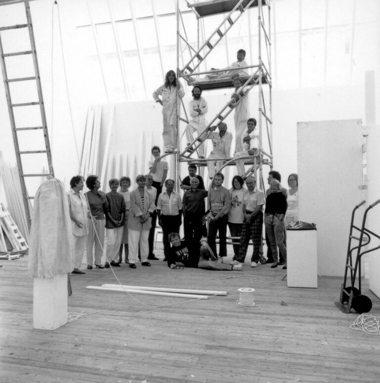 En gruppbild med ett 23 personer. Några står uppe i en byggställning och flera står på golvet. Många är iförda arbetskläder.