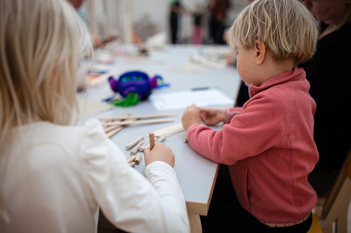 Två barn i åldern 3 till 7 sitter och skapar med vattenfärg, kritor och trämaterial i Konsthallens skapande verkstad.