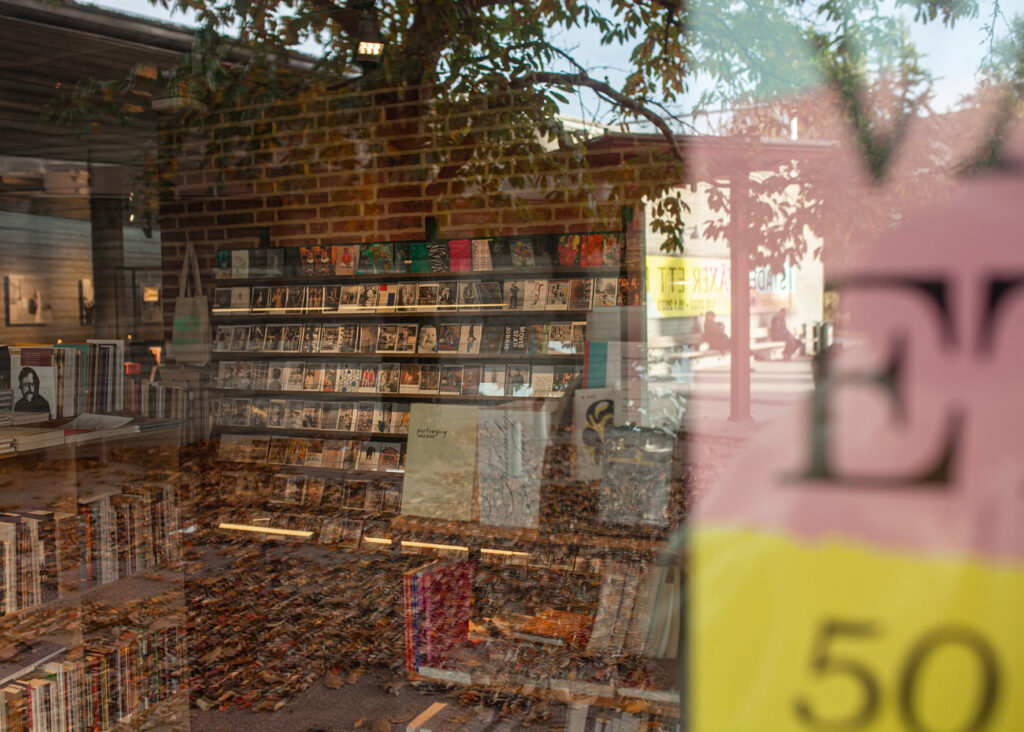 Bild tagen utifrån piazzan in genom bokhandelns fönster, speglingar reflekterar utsidan ovanpå bokhandelns inre.