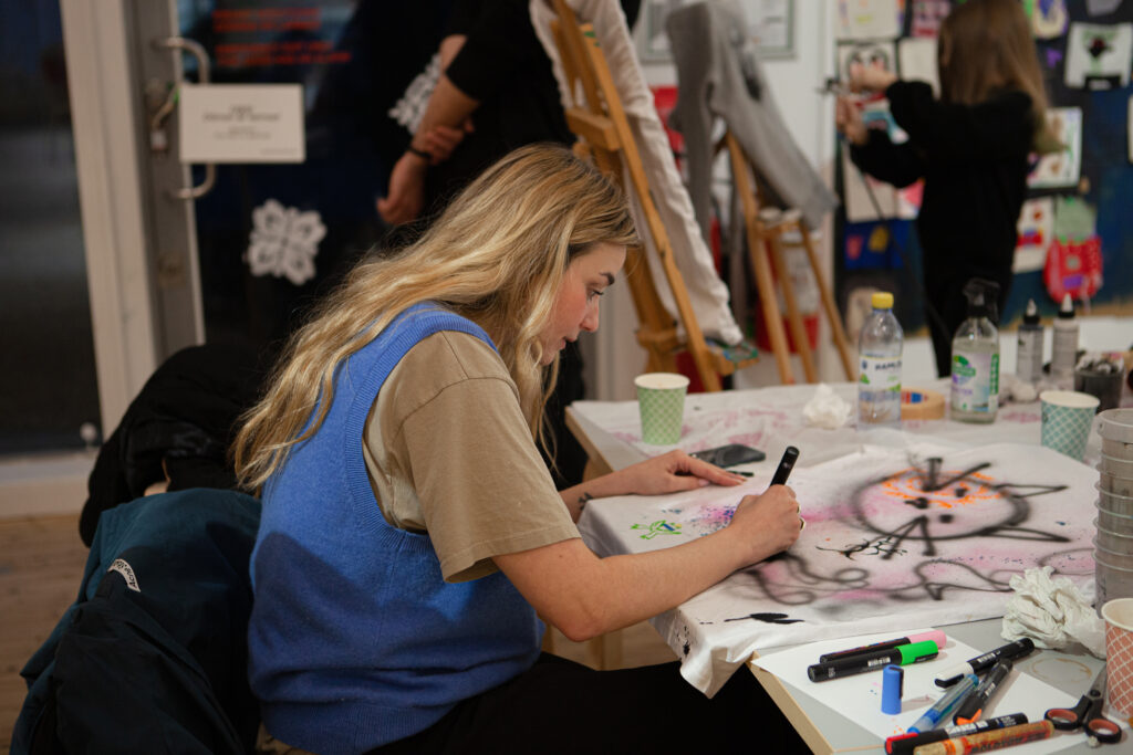 Woman photographed obliquely from above while working on a large drawing on a t-shirt