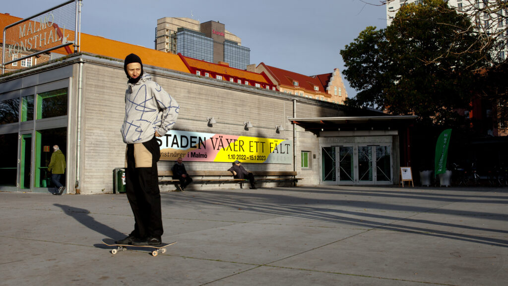 Bild av piazzan utanför Malmö Konsthall och människor i rörelse bland annat en person på skateboard.