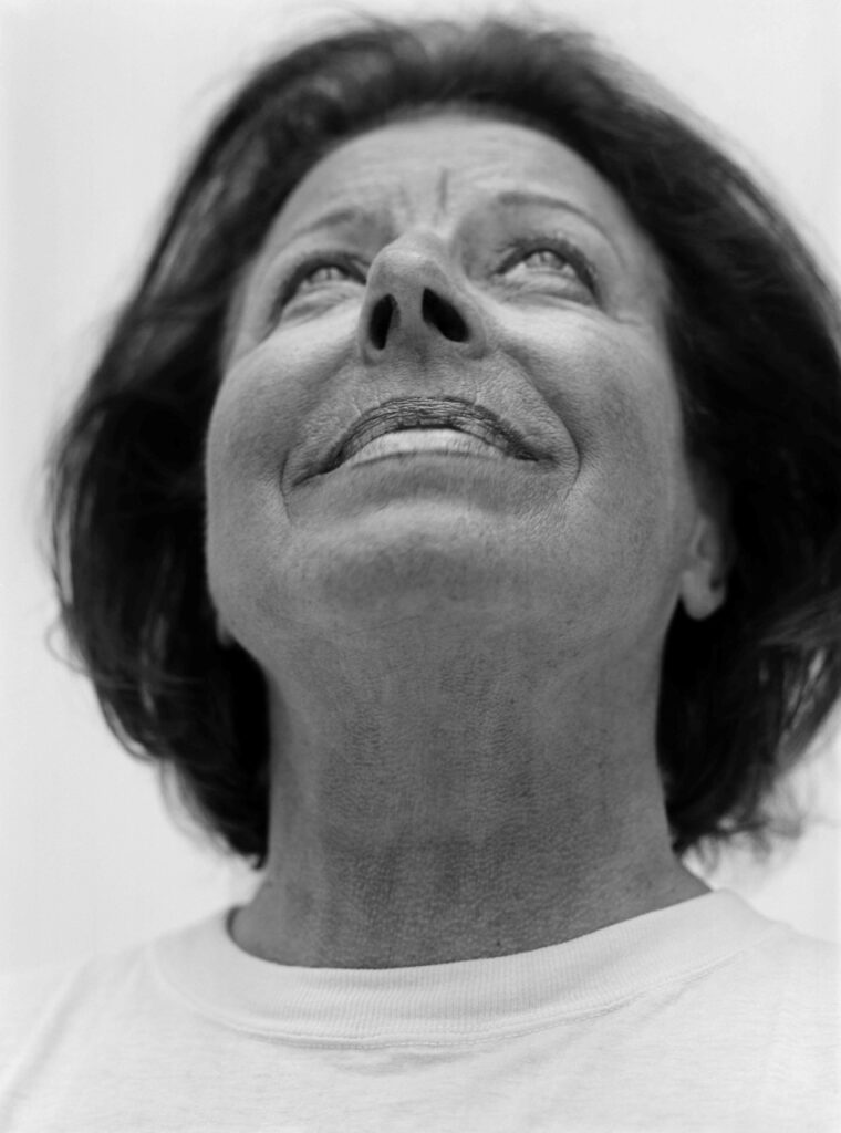 Porträtt av Margaretha Krook i svartvitt. Hon är fotograferad nerifrån och tittar upp mot himlen med ett leende på läpparna.