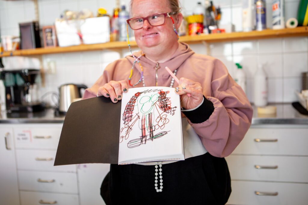 En person håller glatt fram en teckning som hon har ritat.