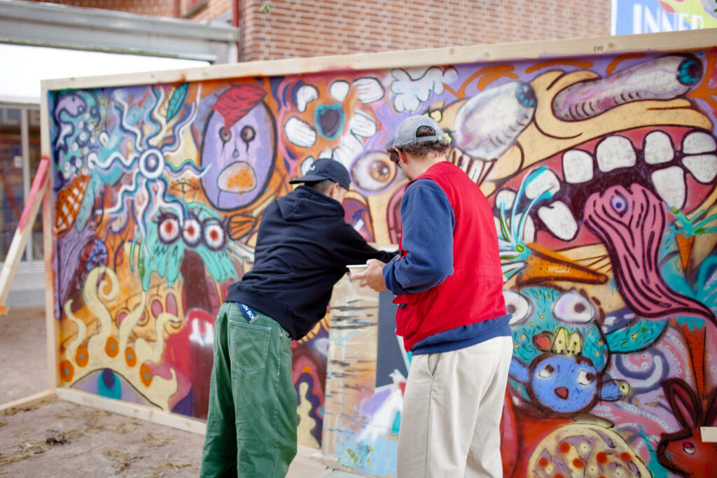 Two young guys in front of a vibrant graffiti wall.