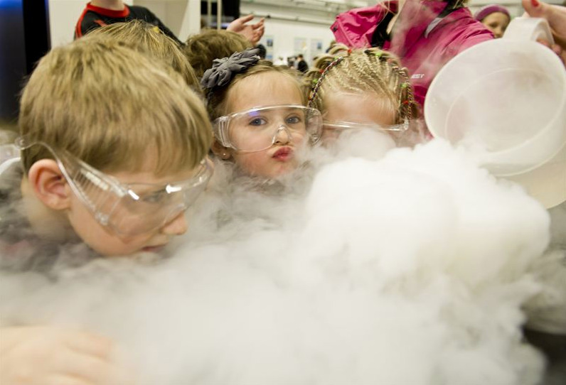 Tre barn i fysiker-glasögon utför ett experiment där det ryker.
