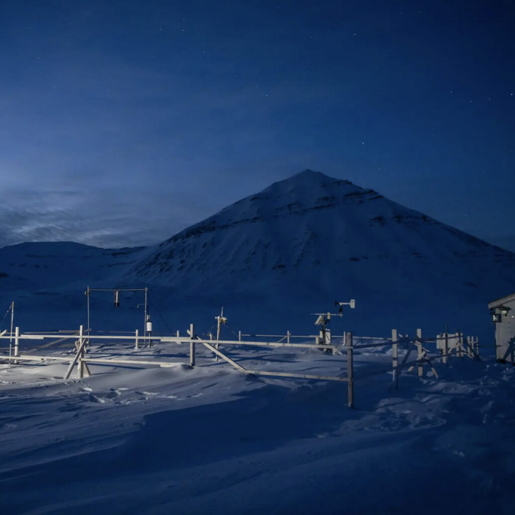 Snow covered research station on a polar night. Measuring tools in the foreground and mountains in the background.