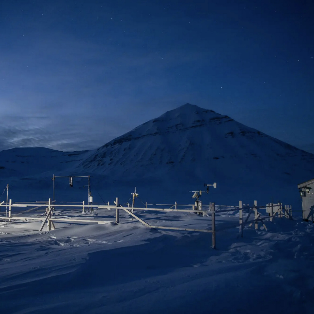 Snötäckt forskningsstation en polarnatt. Mätverktyg i förgrunden och berg i bakgrunden.