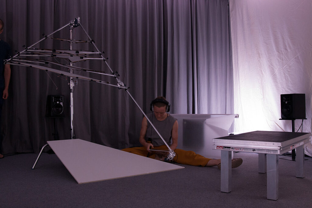 A person sits in a dimly lit room with headphones on in front of a measuring instrument that produces sounds from a climate station in the Arctic.