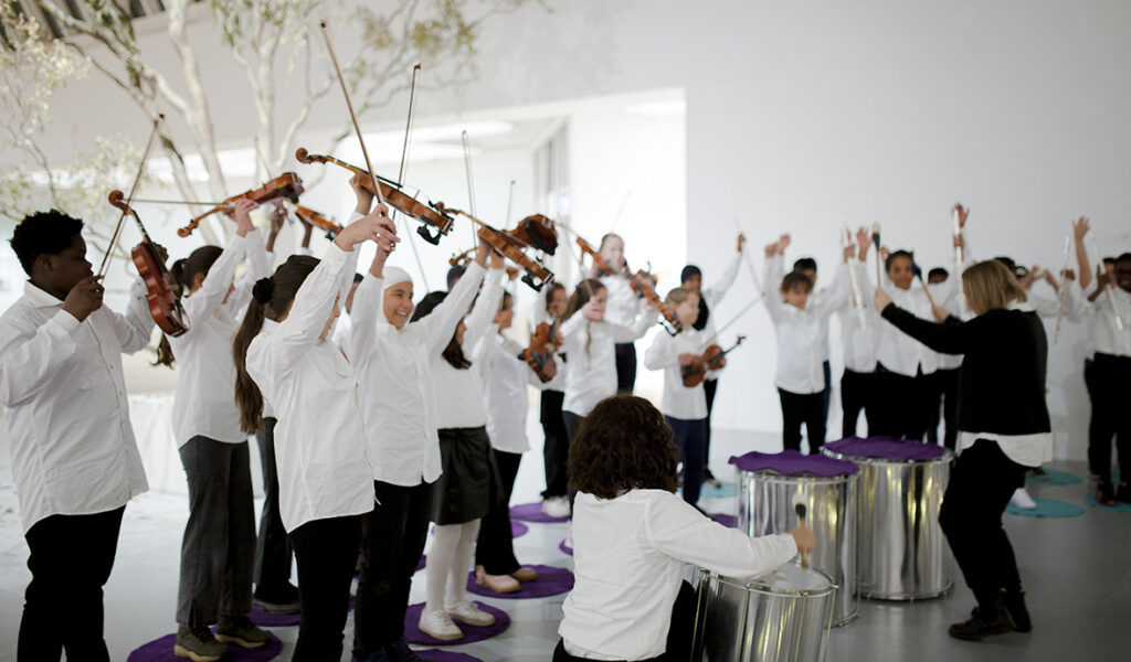 En stor grupp med barn – en kör står i konsthallen och lyfter glatt sina instrument.