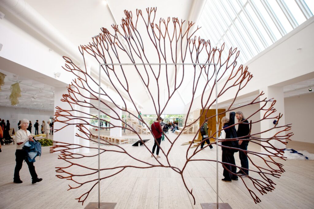 A large artwork depicting seaweed. In the background, people can be seen walking around the exhibition room at Malmö Konsthall.