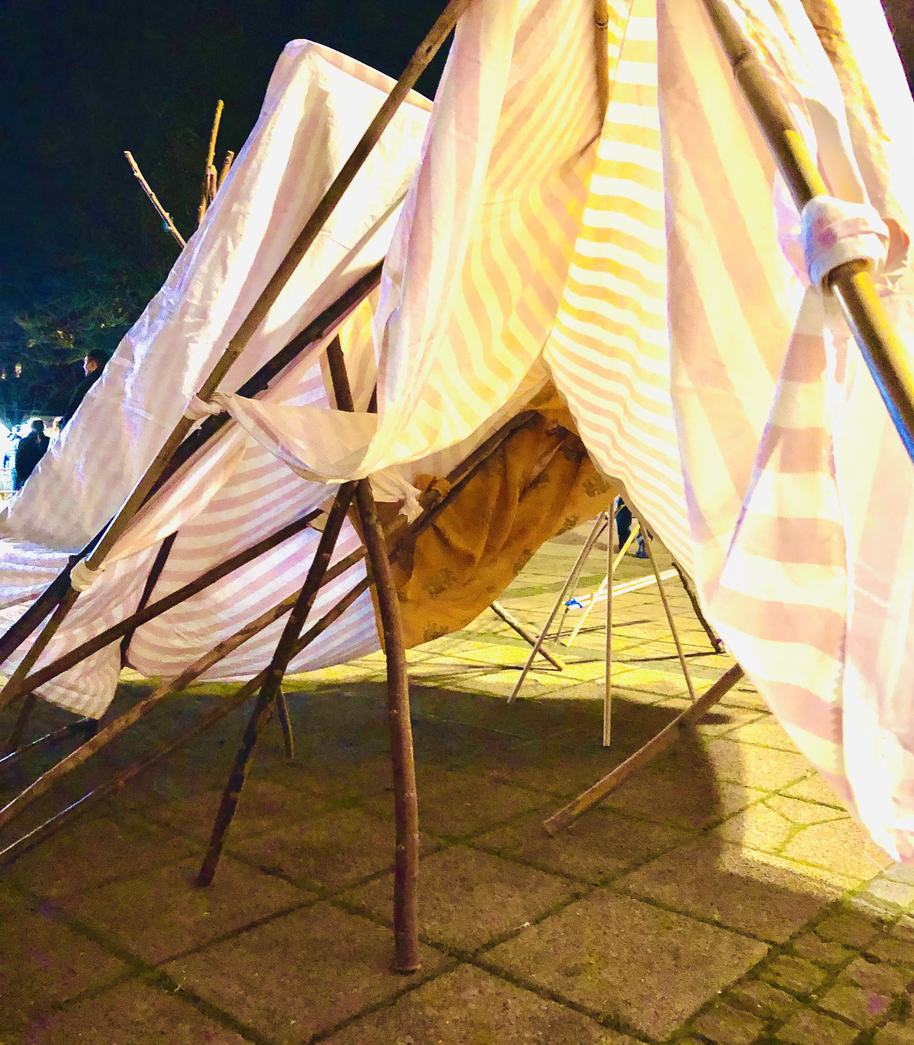 Simple tents built from wooden sticks and fabric. One is yellow and one is pink.