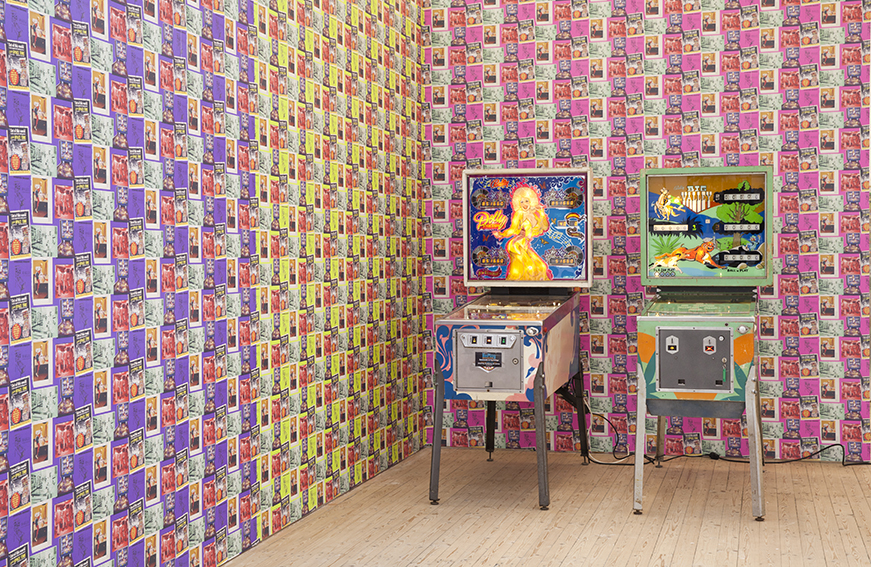 Två flipperspel står i ett rum med färgglada, mönstrade tapeter.