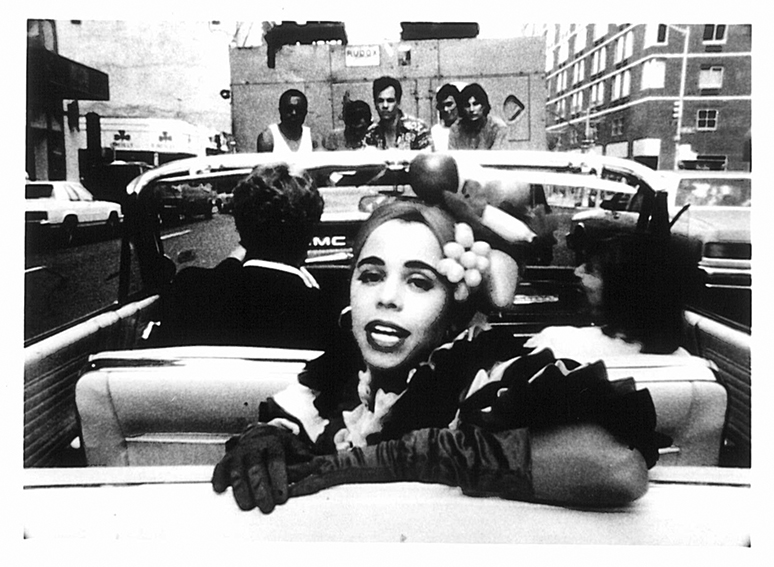 Black and white vintage picture of a provocatively dressed woman looking out of the back seat of a convertible car.